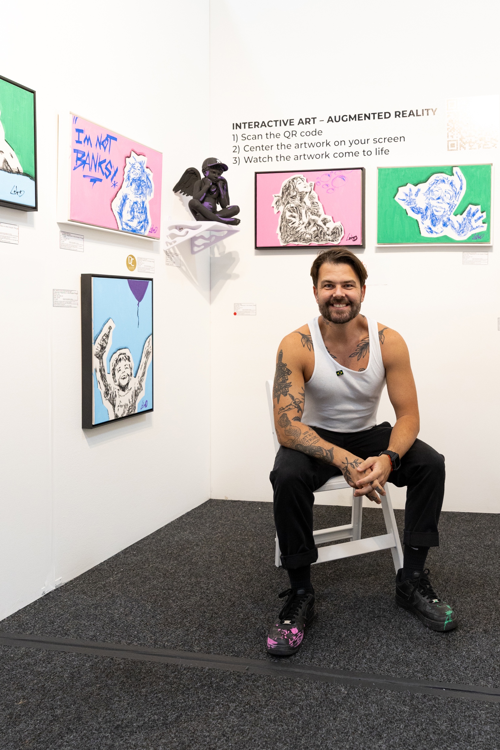 Lito sentado em um espaço de exposição com suas obras em Nova York